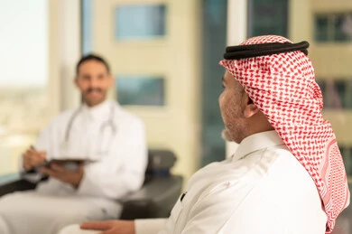 Recording examination results in the medical record of an elderly patient, dealing well with patients, smiling and happy gestures, a Saudi Arabian Gulf doctor wearing traditional thobe and white coat holding patient files, working in the health sector, preparing medical reports