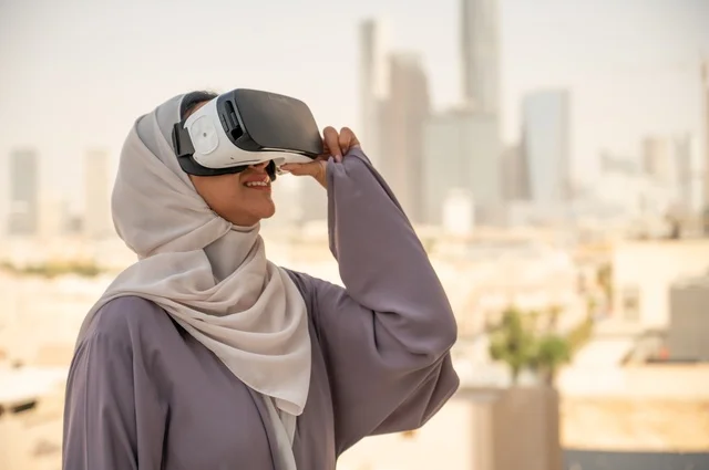 تقنيات حديثة الكترونية وأجهزة تكنولوجية، التفاعل ومحاكاة العالم الافتراضي الخيالي, صورة مقربة من الجانب لامرأة عربية خليجية سعودية محجبة تقف في المعرض تضع نظارات الفي ار, الاستمتاع في قضاء اوقات ترفيهية، قضاء وقت ممتع خارج المنزل