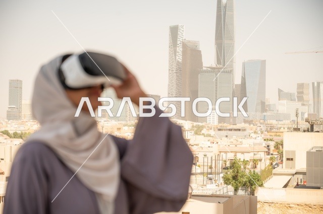 تقنيات حديثة الكترونية وأجهزة تكنولوجية، التفاعل ومحاكاة العالم الافتراضي الخيالي, صورة مقربة من الجانب لامرأة عربية خليجية سعودية محجبة تقف في المعرض تضع نظارات الفي ار, الاستمتاع في قضاء اوقات ترفيهية، قضاء وقت ممتع خارج المنزل