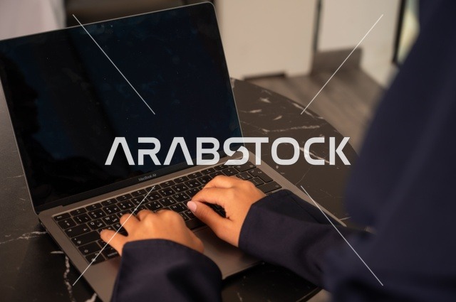 Remote business management, using a modern and advanced technical device, a close-up image of a Saudi Gulf Arab woman wearing an abaya and hijab using a laptop in the office, integrating technology with work, completing required tasks via the laptop, a female office profession and job.