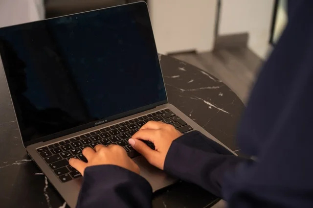 Remote business management, using a modern and advanced technical device, a close-up image of a Saudi Gulf Arab woman wearing an abaya and hijab using a laptop in the office, integrating technology with work, completing required tasks via the laptop, a female office profession and job.
