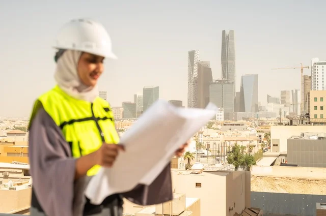 An Arab Saudi Gulf female architect holding a building plan in her hand, a hijab-wearing construction engineer dressed in a work safety suit, a hard hat, formal work attire, a construction project, engineering professions and jobs for women, facial expressions indicating joy, working in the engineering field, the concept of engineering and construction.