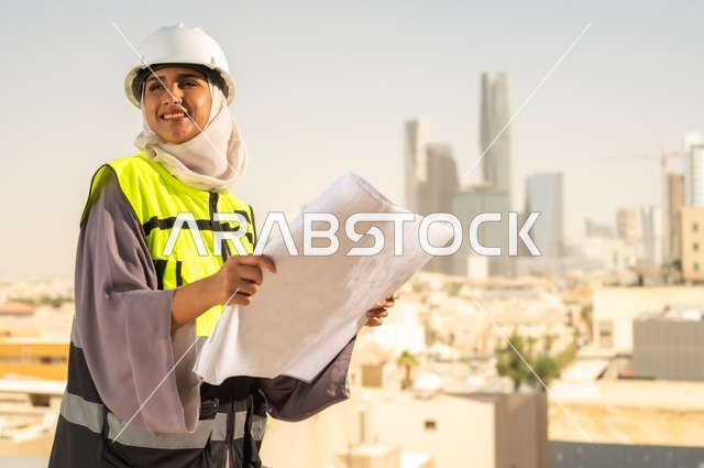 ايماءات السرور والفخر، مهندسة معمارية عربية سعودية خليجية تحمل بيدها مخطط البناء، مهندسة انشاءات محجبة ترتدي بدلة السلامة في العمل ، خوذة العمل، لباس رسمي للعمل، مشروع بناء، مهن ووظائف نسائية هندسية, ايماءات وجه تدل على السرور، مفهوم الهندسة و الإنشاءات