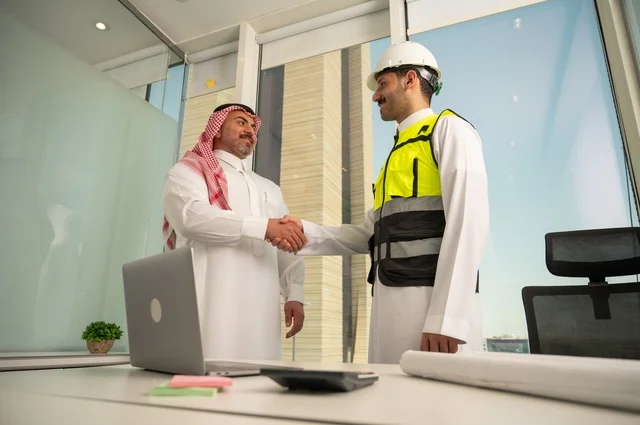 المصافحة والترحيب والاستقبال, مفهوم التعاون والعمل المشترك, مهندس عربي خليجي سعودي يرتدي الخوذة وسترة الحماية يقوم بمصافحة رجل اعمال يرتدي الشماغ و الثوب التقليدي، الاتفاق على الخطط والمشاريع الهندسية في موقع العمل , الإنشاءات المعمارية في الأراضي السعودية