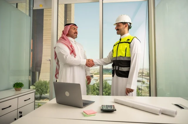 المصافحة والترحيب والاستقبال, مفهوم التعاون والعمل المشترك, مهندس عربي خليجي سعودي يرتدي الخوذة وسترة الحماية يقوم بمصافحة رجل اعمال يرتدي الشماغ و الثوب التقليدي، الاتفاق على الخطط والمشاريع الهندسية في موقع العمل , الإنشاءات المعمارية في الأراضي السعودية