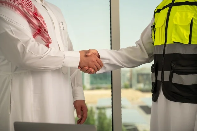 The handshake, greeting, and reception, the concept of cooperation and joint work, a Saudi Gulf Arab engineer wearing a helmet and safety vest shaking hands with a businessman wearing a ghutrah and traditional thobe, agreeing on engineering plans and projects at the work site, architectural constructions in Saudi lands.