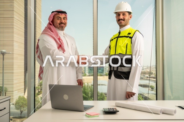 The handshake, greeting, and reception, the concept of cooperation and joint work, a Saudi Gulf Arab engineer wearing a helmet and safety vest shaking hands with a businessman wearing a ghutrah and traditional thobe, agreeing on engineering plans and projects at the work site, architectural constructions in Saudi lands.