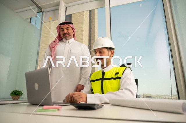 الشركات المختصة بورشات البناء والمقاولات، متابعة تنفيذ الخطط الهندسية الموضوعة مسبقا، التخطيط ووضع اللمسات الأخيرة على المخططات المعمارية، رجل أعمال عربي خليجي سعودي يرتدي الشماغ ومهندس يرتدي الخوذة وسترة الحماية يعملان على مناقشة مخطط الإنشاء وتحديد القياسات بدقة