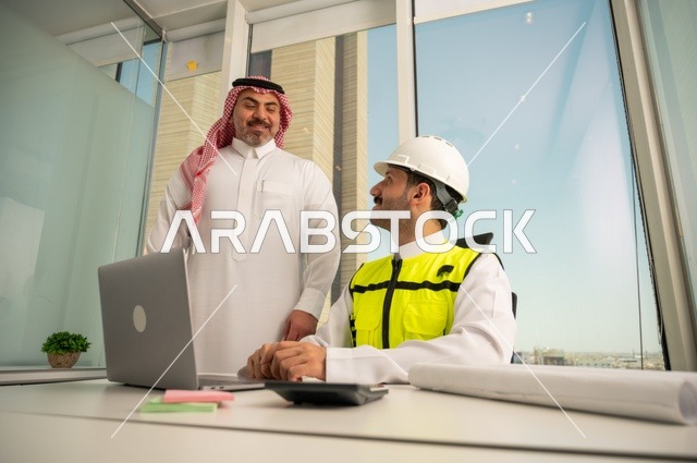 متابعة تنفيذ الخطط الهندسية الموضوعة مسبقا، الشركات المختصة بورشات البناء والمقاولات، التخطيط ووضع اللمسات الأخيرة على المخططات المعمارية، رجل أعمال عربي خليجي سعودي يرتدي الشماغ ومهندس يرتدي الخوذة وسترة الحماية يعملان على مناقشة مخطط الإنشاء وتحديد القياسات بدقة