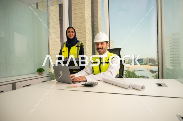 دمج التكنولوجيا والأجهزة التقنية في الحياة العملية، التعاون لإنجاز العمل بسرعة ودقة, الإشراف والمناقشة على المشاريع الهندسية من مكتب هندسي،  مهندسان عربيان خليجيان سعوديان يرتديان سترة العمل و يقومان بدراسة و تقييم الخطط الهندسية من خلال الحاسوب المحمول