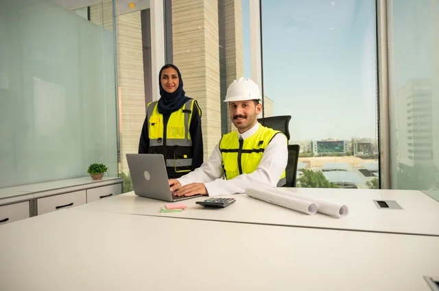 دمج التكنولوجيا والأجهزة التقنية في الحياة العملية، التعاون لإنجاز العمل بسرعة ودقة, الإشراف والمناقشة على المشاريع الهندسية من مكتب هندسي،  مهندسان عربيان خليجيان سعوديان يرتديان سترة العمل و يقومان بدراسة و تقييم الخطط الهندسية من خلال الحاسوب المحمول