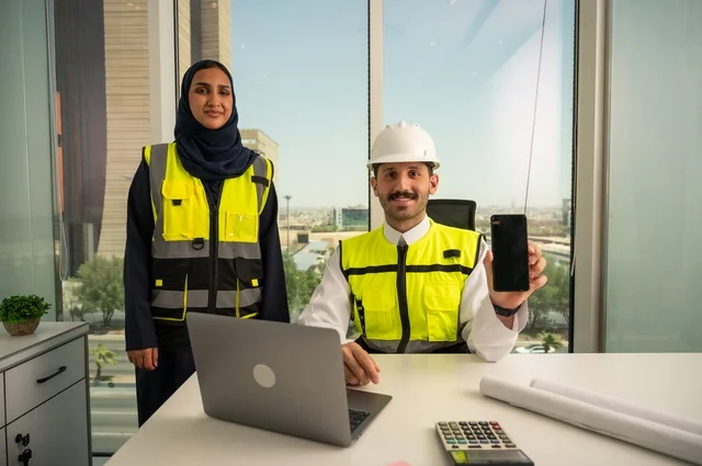 يعرض المهندس خلفية هاتف محمول سوداء، مهندسان عربيان خليجيان سعوديان يرتديان سترة العمل و يقومان بالعمل من خلال الحاسوب المحمول، دمج التكنولوجيا والأجهزة التقنية في الحياة العملية، التعاون لإنجاز العمل بسرعة ودقة, الإشراف والمناقشة على المشاريع الهندسية