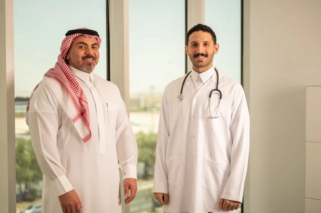 مفهوم الفحص الطبي، العمل في القطاع الصحي، تقديم الخدمات العلاجية للمرضى, طبيب عربي خليجي سعودي يرتدي الثوب التقليدي والمعطف الطبي يضع السماعة الطبية يقف مع مريضه ويعمل في المراكز الصحية والمستشفيات