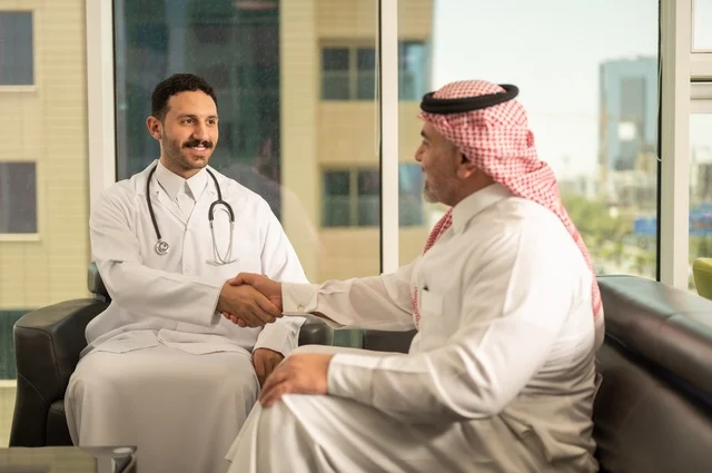 المصافحة والقاء التحية والسلام، مفهوم الفحص الطبي، العمل في القطاع الصحي، تقديم الخدمات العلاجية للمرضى, طبيب عربي خليجي سعودي يرتدي الثوب التقليدي والمعطف الطبي يضع السماعة الطبية يقوم بمصافحة مريضه العمل في المراكز الصحية والمستشفيات