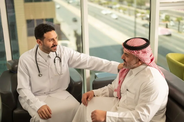 مفهوم الفحص الطبي، العمل في القطاع الصحي، تقديم الخدمات العلاجية للمرضى, طبيب عربي خليجي سعودي يرتدي الثوب التقليدي والمعطف الطبي يضع السماعة الطبية يجلس مع مريضه ويعمل في المراكز الصحية والمستشفيات