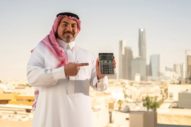 The concept of facilitating business and the ability to accomplish tasks, using modern technologies and advanced devices, a Saudi Arabian Gulf man wearing traditional clothing holding a calculator to perform calculations, a background of towers and skyscrapers in Riyadh