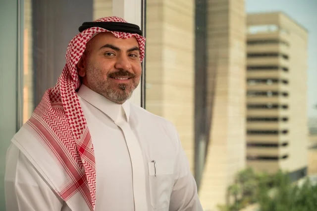 الاناقة والاهتمام بالمظهر الخارجي. صورة مقربة لرجل عربي خليجي سعودي مبتسم يرتدي الثوب والشماغ التقليدي ينظر الى الكاميرا بايماءات السرور والسعادة. الخروج في الهواء الطلق،  مفهوم الرجولة والثقة بالنفس، خلفية أبنية