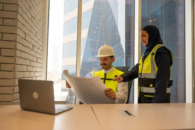 الإشراف والنقاش في العمل، مهندسان معماريان سعوديان خليجيان يحملان مخطط لمشروع البناء للتخطيط وتنفيذ العمل في داخل المكتب في المملكة العربية السعودية, إرتداء سترة الحماية الخاصة بالعمل, تدقيق العمل،  مفهوم الهندسة، مهن ووظائف هندسية،دمج التكنولوجيا في العمل