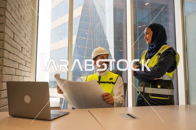 مهنة ووظيفة مكتبية سعودية، مهندسان معماريان سعوديان خليجيان يحملان مخطط لمشروع البناء للتخطيط وتنفيذ العمل في داخل المكتب, إرتداء سترة الحماية الخاصة بالعمل, تدقيق العمل،  كتابة وتدوين البيانات والنتائج، ادارة وانجاز المهام باستخدام جهاز تقني حديث ومتطور