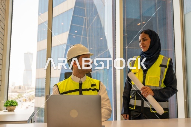 Work auditing, managing and completing tasks using modern and advanced technical devices, a profession and office job in Saudi Arabia, two Saudi Gulf architects holding a plan for a construction project to plan and execute work inside the office, wearing work safety vests, writing and recording data and results.