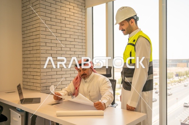 مفهوم الهندسة والإنشاءات المعمارية, مشاريع إعمارية سعودية وطنية، التفاهم والتعاون بين الزملاء، مهندس عربي خليجي سعودي يرتدي سترة العمل وخوذة الحماية البيضاء مع زميله يقرأوا المخططات الهندسية يقوموا بتدوين الملاحظات باستخدام الأجهزة التقنية الحديثة
