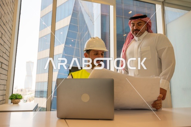 مهندس عربي خليجي سعودي يرتدي سترة العمل وخوذة الحماية البيضاء مع زميله يقرأوا المخططات الهندسية يقوموا بتدوين الملاحظات باستخدام الأجهزة التقنية الحديثة، التفاهم والتعاون بين الزملاء، مفهوم الهندسة والإنشاءات المعمارية, مشاريع إعمارية سعودية وطنية