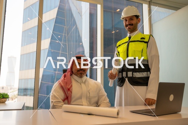 اجتماع في مكتب العمل، ايماءات السعادة والسرور،الاتفاق والشراكة على الأعمال والمشاريع، عقد صفقات عمل جديدة، تصوير من الجانب لرجل عربي خليجي سعودي يرتدي الثوب والشماغ مع زميله مهندس يرتدي الخوذة وسترة الحماية,  مشاريع إعمارية سعودية وطنية
