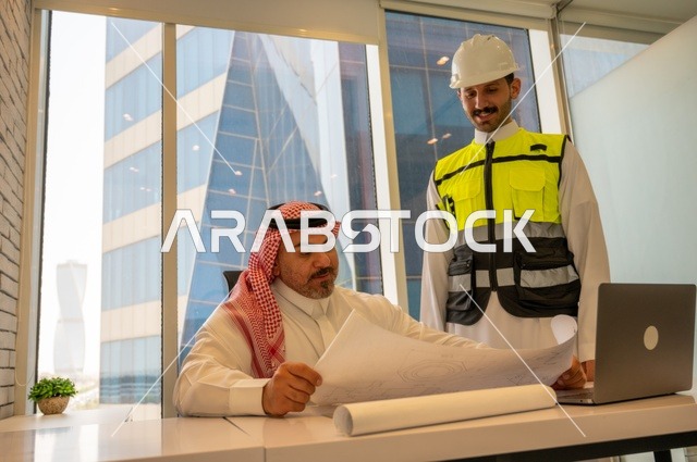 مهندس عربي خليجي سعودي يرتدي سترة العمل وخوذة الحماية البيضاء مع زميله يقرأوا المخططات الهندسية يقوموا بتدوين الملاحظات باستخدام الأجهزة التقنية الحديثة، التفاهم والتعاون بين الزملاء، مفهوم الهندسة والإنشاءات المعمارية, مشاريع إعمارية سعودية وطنية