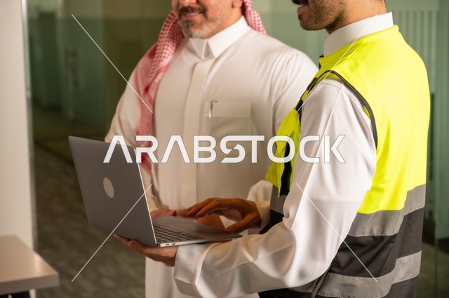 التفاهم والتعاون بين الزملاء، عقد صفقات عمل جديدة، تبادل الخبرات والمعلومات لتحقيق الاهداف، صورة مقربة لمهندس عربي خليجي سعودي يرتدي سترة العمل وخوذة الحماية البيضاء يقف مع زميله، مفهوم الهندسة والإنشاءات المعمارية، مشاريع إعمارية سعودية وطنية