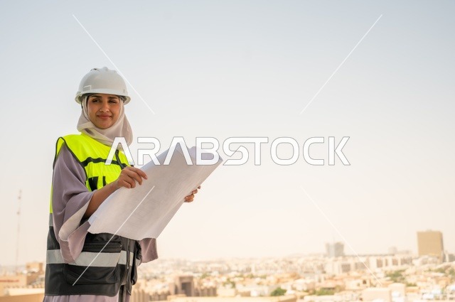 Construction project, side view of a Saudi Arabian Gulf female architect holding a building plan in her hand, a smiling hijab-wearing construction engineer dressed in work safety gear, a work helmet, formal work attire, female engineering professions and jobs, background of towers and skyscrapers.