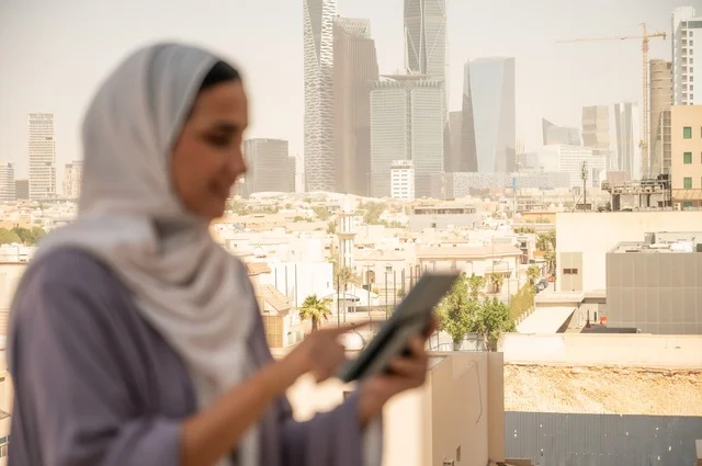 استخدام جهاز تقني حديث ومتطور، صورة مقربة لامرأة عربية خليجية عربية سعودية ترتدي العباءة والحجاب تقوم باستخدام الهاتف المحمول،التواصل مع العملاء عن بعد، دمج التكنولوجيا بالعمل، إنجاز المهام المطلوبة اليومية، مهنة ووظيفة نسائية مكتبية
