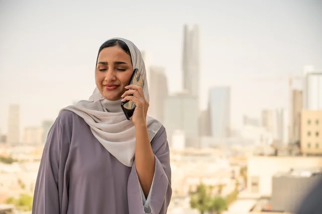 إجراء اتصال هاتفي عبر الجوال, استخدام جهاز تقني حديث ومتطور في العمل, مهنة ووظيفة مكتبية في السعودية, امرأة عربية خليجية سعودية محجبة ترتدي العباءة تقف في الهواء الطلق وتمسك الهاتف المحمول بيدها,التواصل مع العملاء عن بعد