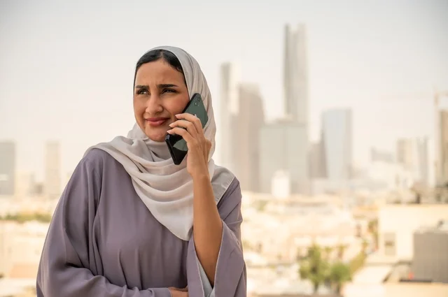 استخدام جهاز تقني حديث ومتطور، صورة مقربة لامرأة عربية خليجية عربية سعودية ترتدي العباءة والحجاب تقوم باستخدام الهاتف المحمول،التواصل مع العملاء عن بعد، دمج التكنولوجيا بالعمل، إنجاز المهام المطلوبة اليومية، مهنة ووظيفة نسائية مكتبية