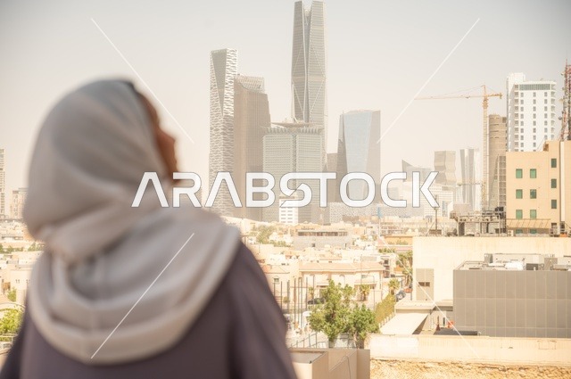 تأمل التطور العمراني في المدينة، صورة صورة خلفية لامرأة عربية خليجية عربية سعودية ترتدي العباءة والحجاب تقف في الهواء الطلق، إنجاز المهام المطلوبة اليومية، مهنة ووظيفة نسائية مكتبية، الاستمتاع في وقت الفراغ