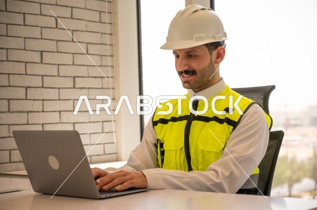 Integrating work with technology and tech, reviewing new engineering designs on a laptop, an Arab Saudi Gulf architect wearing work attire, supervising the implementation of architectural engineering projects and plans in construction.