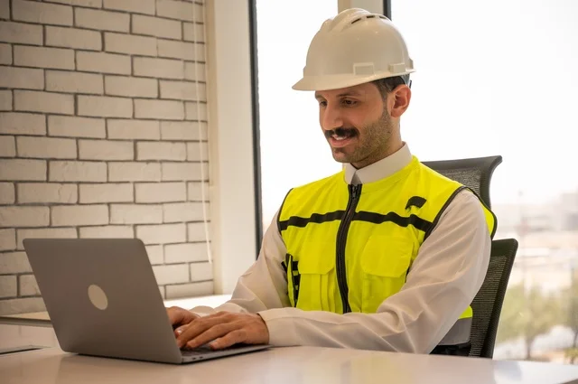 دمج العمل مع التقنية و التكنولوجيا، الاطلاع على تصاميم هندسية جديدة على جهاز الحاسوب المحمول، مهندس معماري عربي سعودي خليجي يرتدي اللباس الخاص بالعمل، الاشراف على تطبيق المشاريع و الخطط الهندسيه المعمارية في البناء