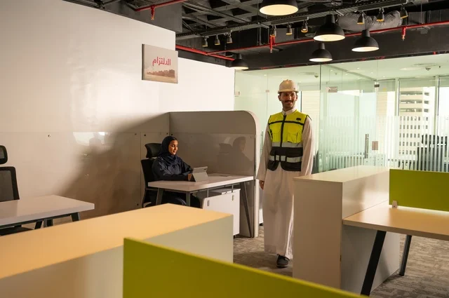 Study and analysis of new projects, use of modern technical devices, unity and teamwork, work development and problem-solving, a Saudi Gulf Arab engineer wearing a work vest and safety helmet inside the company premises, workshops and training, a Saudi office profession and job, exchange of experiences and ideas.
