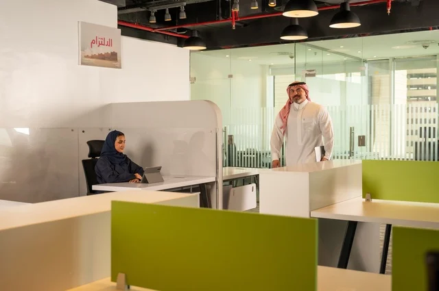 A Saudi office profession and job, a Gulf Arab Saudi man walking inside the company headquarters carrying a laptop, workshops and training, developing, studying, and analyzing new projects, unity and teamwork, analyzing results and charts, developing work and problem-solving.