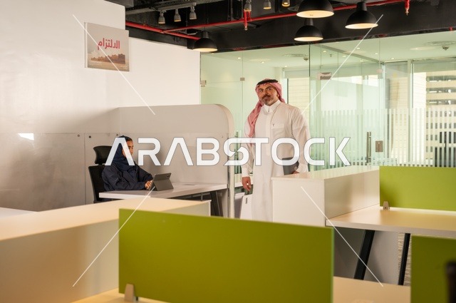 تطوير ودراسة وتحليل المشاريع الجديدة، الوحدة والعمل الجماعي، ورش عمل وتدريب، تحليل النتائج والرسوم البيانية، مهنة ووظيفة سعودية مكتبية، تطوير العمل وحل المشكلات،رجل خليجي عربي سعودي يسير داخل مقر الشركة حاملا الحاسب المحمول