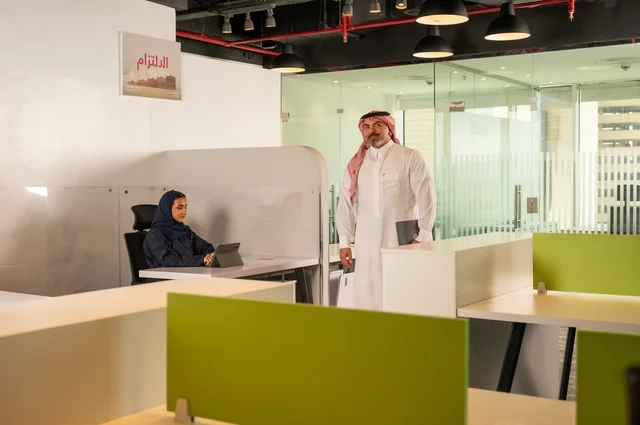 Development, study, and analysis of new projects, unity and teamwork, workshops and training, analysis of results and charts, a Saudi office profession and job, work development and problem-solving, a Gulf Arab Saudi man walking inside the company headquarters carrying a laptop.