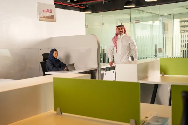 ورش عمل وتدريب، تطوير ودراسة وتحليل المشاريع الجديدة، الوحدة والعمل الجماعي، تحليل النتائج والرسوم البيانية، مهنة ووظيفة سعودية مكتبية، تطوير العمل وحل المشكلات،رجل خليجي عربي سعودي يسير داخل مقر الشركة حاملا الحاسب المحمول