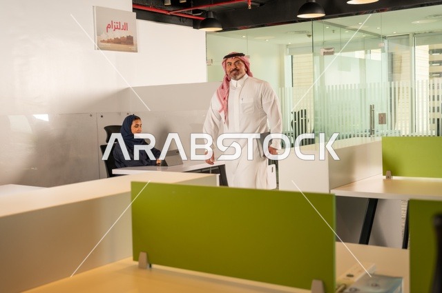 رجل خليجي عربي سعودي يسير داخل مقر الشركة حاملا الحاسب المحمول، ورش عمل وتدريب، تطوير ودراسة وتحليل المشاريع الجديدة، الوحدة والعمل الجماعي، تحليل النتائج والرسوم البيانية، مهنة ووظيفة سعودية مكتبية، تطوير العمل وحل المشكلات