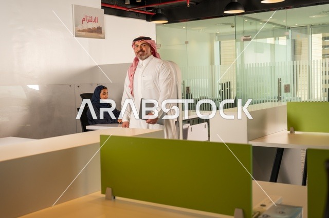 تطوير ودراسة وتحليل المشاريع الجديدة، الوحدة والعمل الجماعي، ورش عمل وتدريب، تحليل النتائج والرسوم البيانية، مهنة ووظيفة سعودية مكتبية، تطوير العمل وحل المشكلات،رجل خليجي عربي سعودي يسير داخل مقر الشركة حاملا الحاسب المحمول