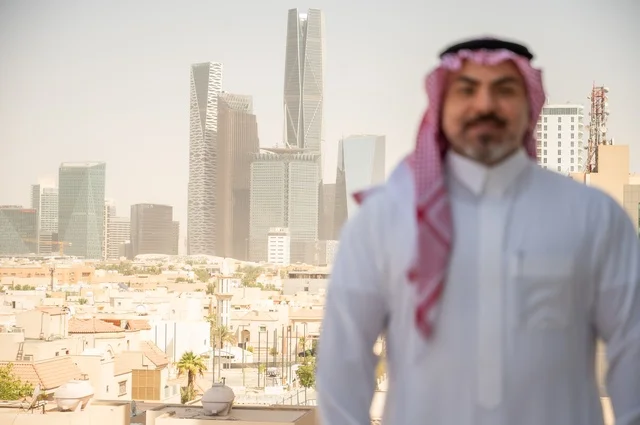 الاناقة والاهتمام بالمظهر الخارجي. صورة مقربة لرجل عربي خليجي سعودي مبتسم يرتدي الثوب والشماغ التقليدي ينظر الى الكاميرا بايماءات السرور والسعادة. الخروج في الهواء الطلق،  مفهوم الرجولة والثقة بالنفس، خلفية أبنية