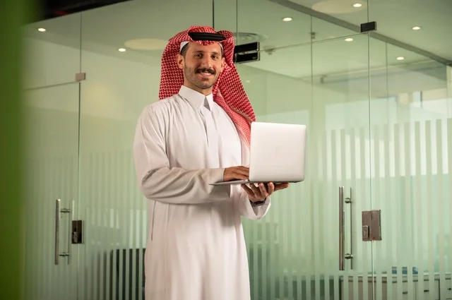 استخدام جهاز تقني حديث ومتطور، إدارة شؤون الأعمال وتنظيمها،  مهنة ووظيفة ادارية مكتبية، رجل عربي خليجي سعودي يرتدي الثوب التقليدي والشماغ يقوم بالعمل على الحاسوب المحمول داخل المكتب، الشركات والمكاتب في المملكة العربية السعودية