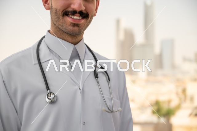 قياس معدل ضربات القلب من خلال سماعة الطبيب، تسجيل الكشوفات والحالات، العمل في القطاعات الصحية، تسجيل التقارير والحالات الصحيه, صورة مقربة لطبيب عربي خليجي سعودي مبتسم يرتدي المعطف الأبيض يقف في الهواء الطلق، خلفية أبراج وناطحات سحاب في الرياض