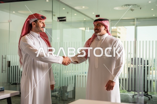 صداقات وتعارف وبناء علاقات اجتماعية، عقد صفقات عمل جديدة ناجحة بين رجال الأعمال، رجلان سعوديان عربيان خليجيان يرتديان الزي التقليدي يقومان بمصافحة بعضهما، توسيع مجالات العمل, الشراكة في الأعمال والمشاريع الهندسية