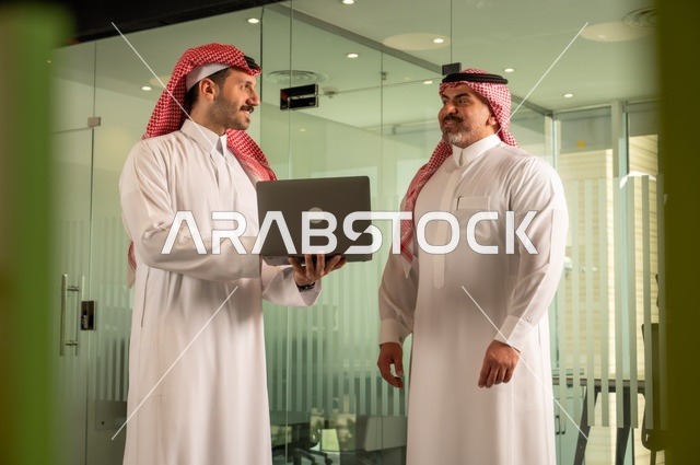 رجل اعمال يرتدي الشماغ و الثوب التقليدي،  مفهوم التعاون والعمل المشترك, صداقات وتعارف وبناء علاقات اجتماعية، عقد صفقات عمل جديدة ناجحة بين رجال الأعمال، رجلان سعوديان عربيان خليجيان يرتديان الزي التقليدي يقومون بالعمل على الحاسب المحمول، توسيع مجالات العمل