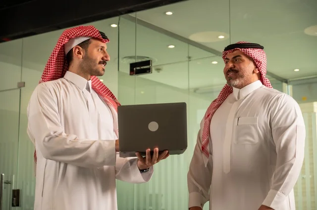 عقد صفقات عمل جديدة ناجحة بين رجال الأعمال،  مفهوم التعاون والعمل المشترك, صداقات وتعارف وبناء علاقات اجتماعية، صورة مقربة لرجلان سعوديان عربيان خليجيان يرتديان الزي التقليدي يقومون بالعمل على الحاسب المحمول، رجل اعمال يرتدي الشماغ و الثوب التقليدي