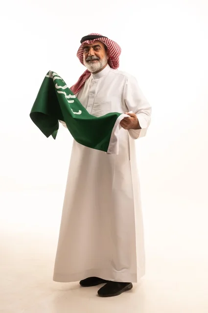 إيماءات الفخر و السرور بالانتماء للوطن, إحياء ذكرى اليوم الوطني السعودي 23 سبتمبر, بورتريه لرجل عربي خليجي سعودي مبتسم يرتدي الشماغ و الثوب التقليدي يحمل بيده علم يوم التأسيس، يوم بدينا 1727 م، الجسم بالطول الكامل، خلفية بيضاء